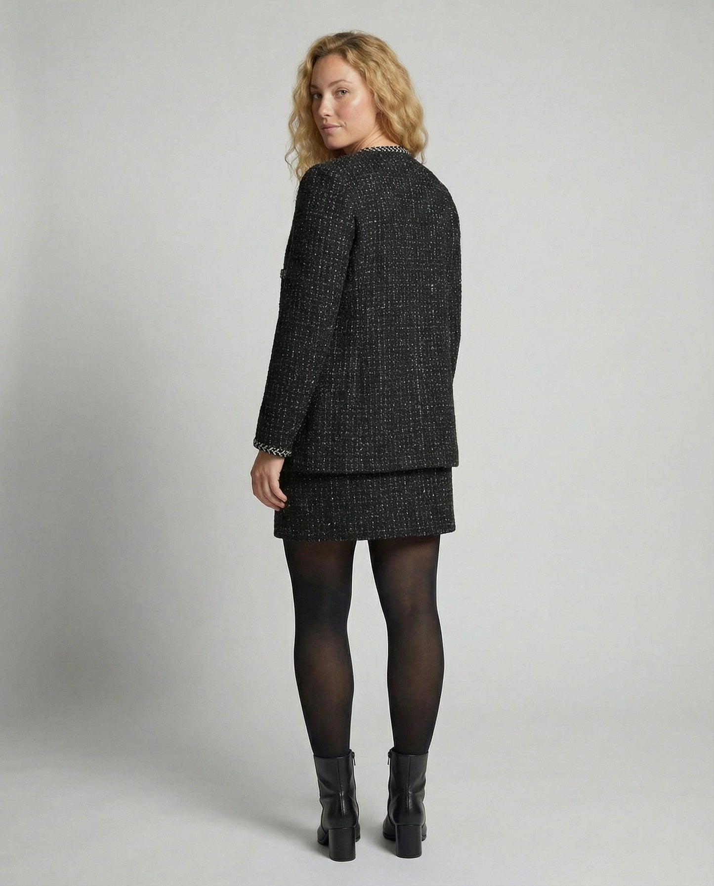 Woman wearing a black tweed suit on a plain background