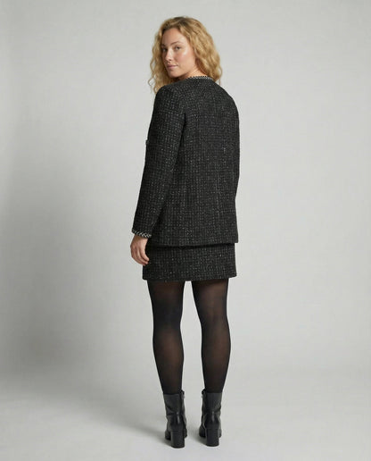 Woman wearing a black tweed suit on a plain background