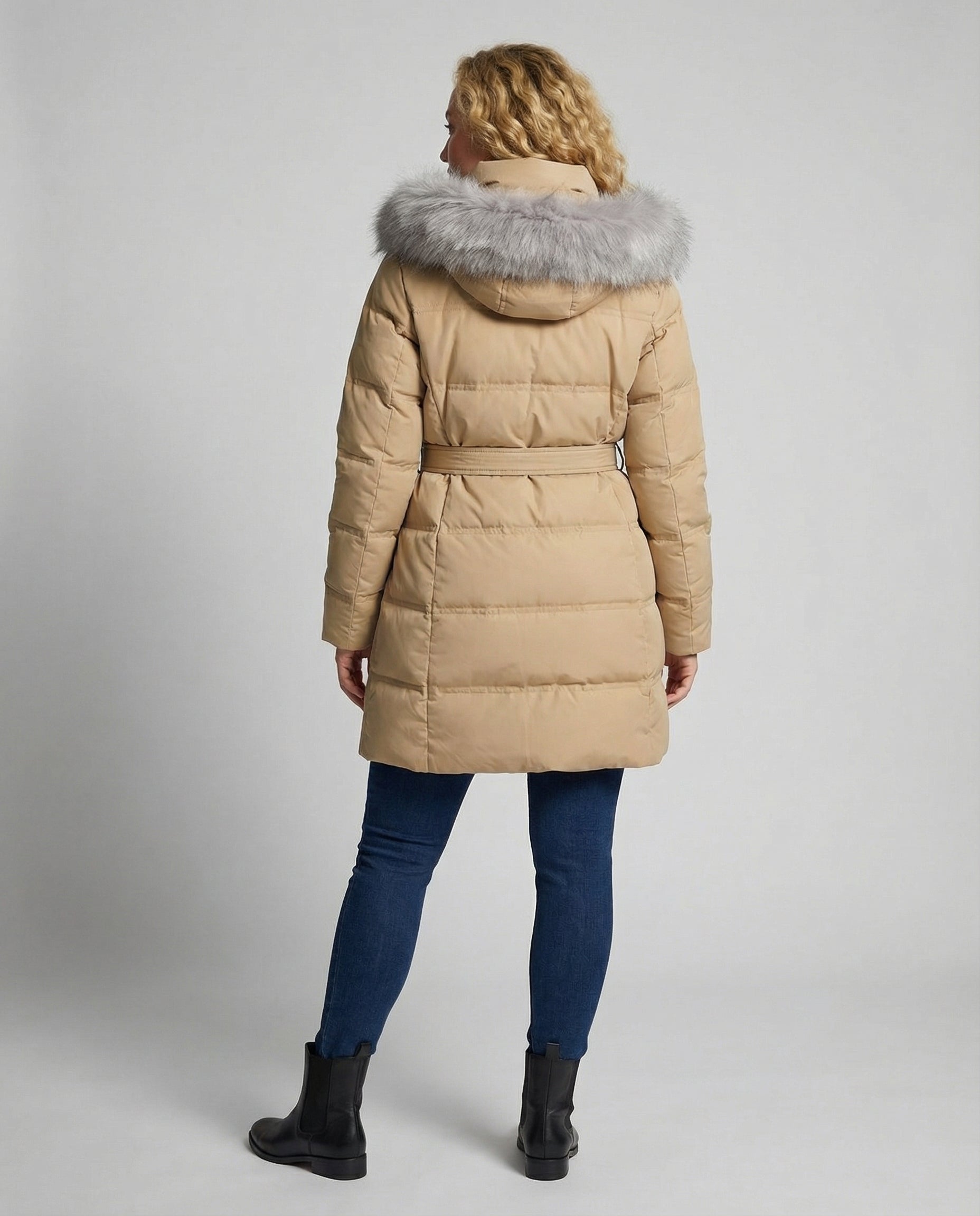 Woman wearing a beige puffer coat with a fur hood on a plain background