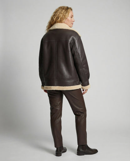 Person wearing a brown leather jacket with shearling collar and cuffs on a gray background