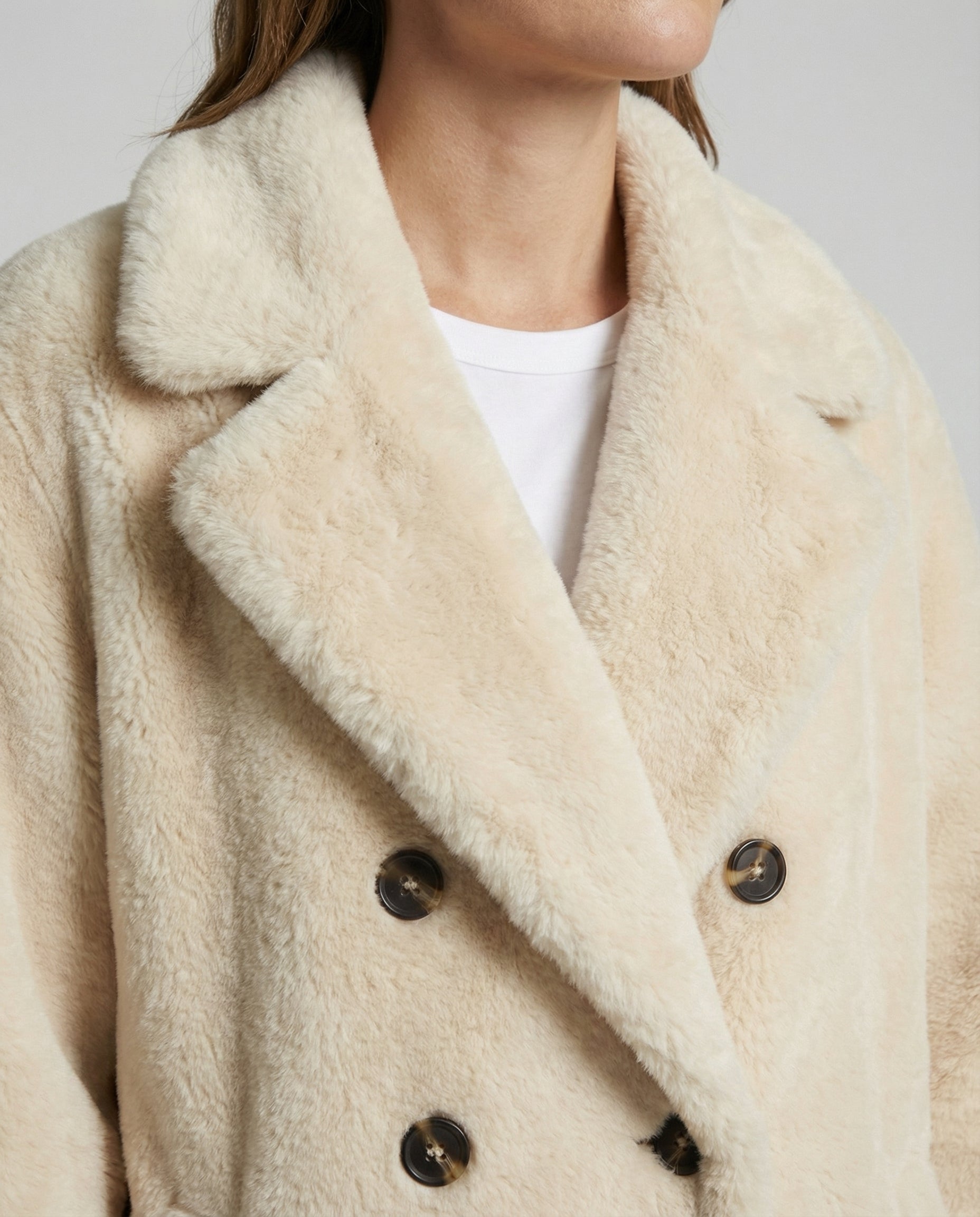 Close-up of a person wearing a beige sherpa coat with a white shirt underneath.