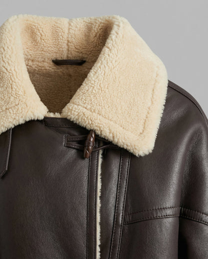 Close-up of a leather jacket with a cream-colored fur collar on a gray background