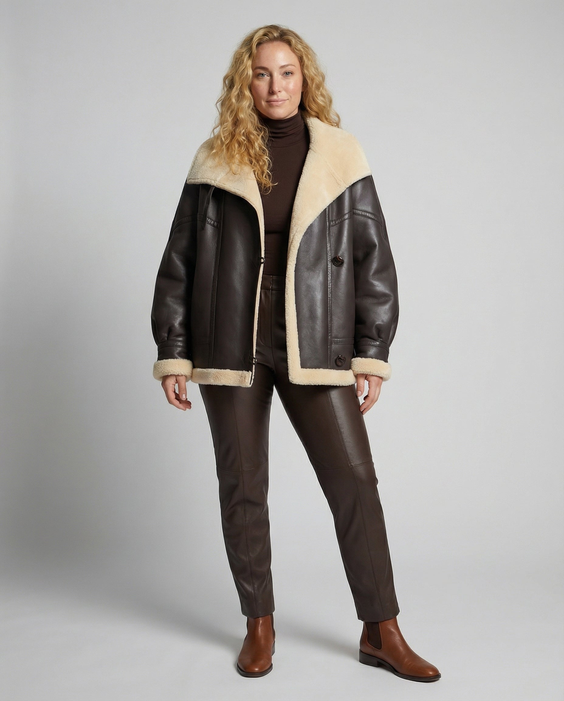 Woman wearing a brown leather jacket with beige fur lining on a gray background