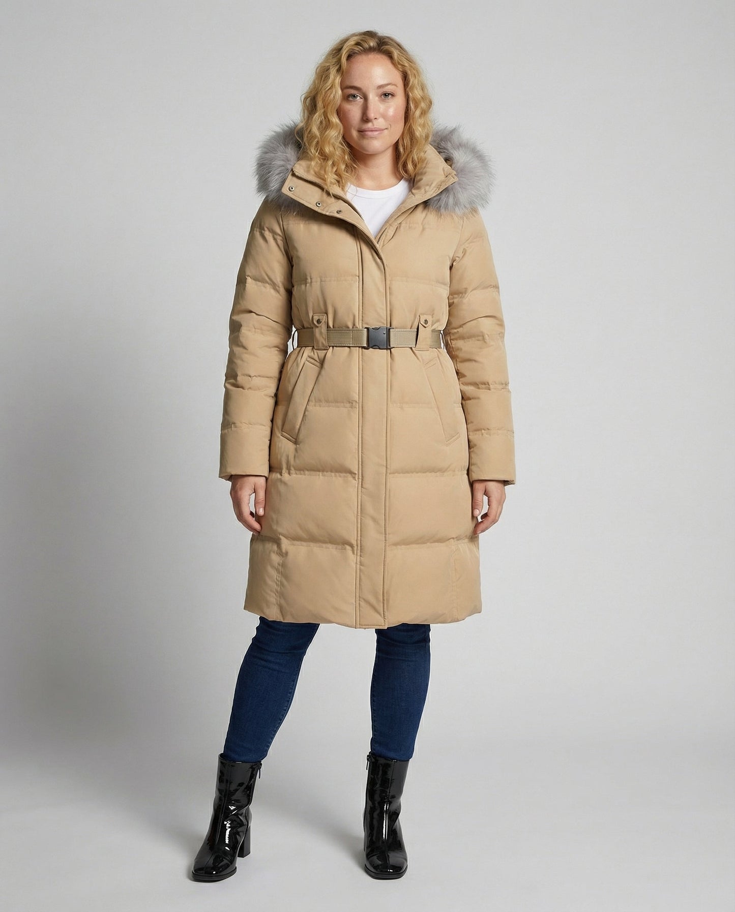 Woman wearing a beige puffer coat with fur hood on a gray background