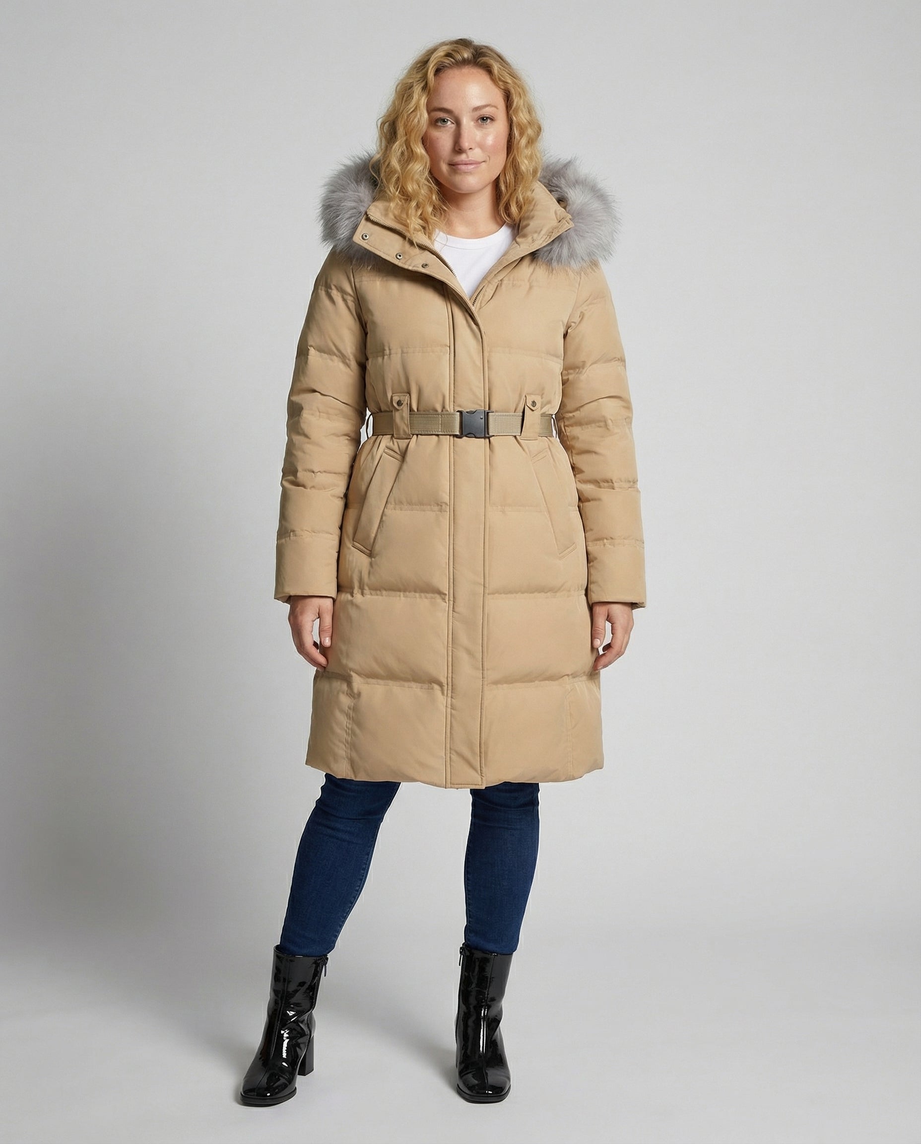 Woman wearing a beige puffer coat with fur hood on a gray background